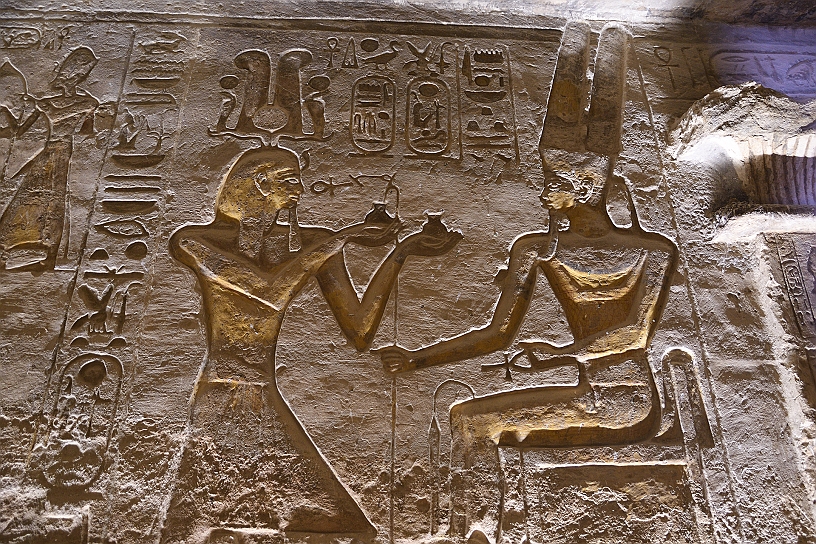 42 MAK_6577.jpg - Ramses II che indossa una corona elaborata con piume e cobra sacri, nell'atto di offrire incenso alla dea Hathor seduta. L'offerta simboleggia il mantenimento dell'ordine divino da parte del sovrano.